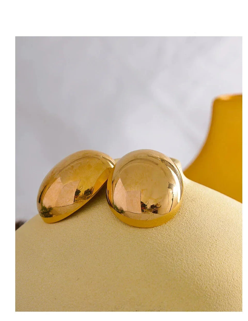 Pair of round, polished 18K gold-plated dome earrings on a soft beige display