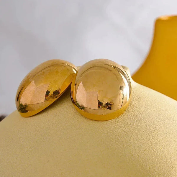 Pair of round, polished 18K gold-plated dome earrings on a soft beige display
