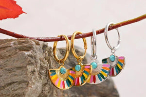 Colorful fan-shaped enamel drop earrings in gold and silver, displayed on a branch.