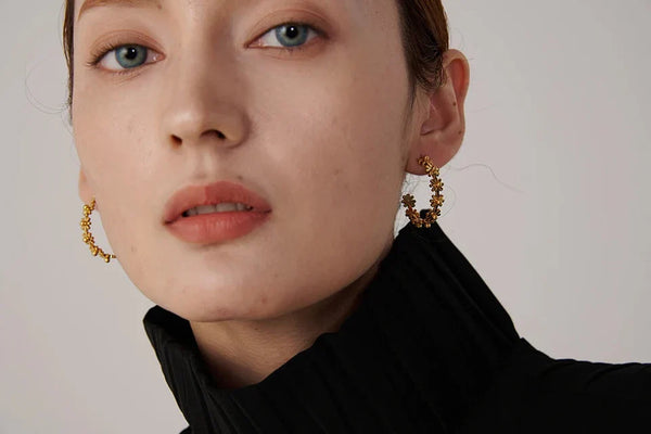 Close-up of a person wearing gold hoop earrings with a neutral background