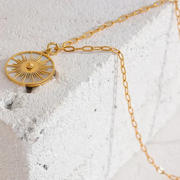Gold necklace with a decorative pendant on a textured white surface