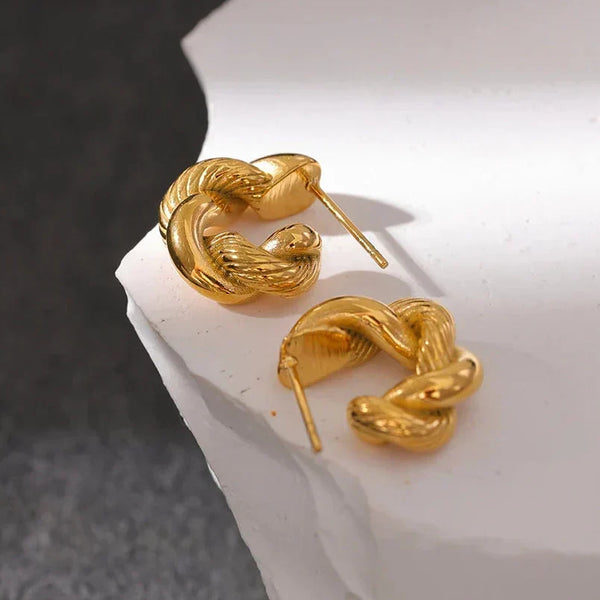 Gold snake-shaped earrings on a white surface with a dark background