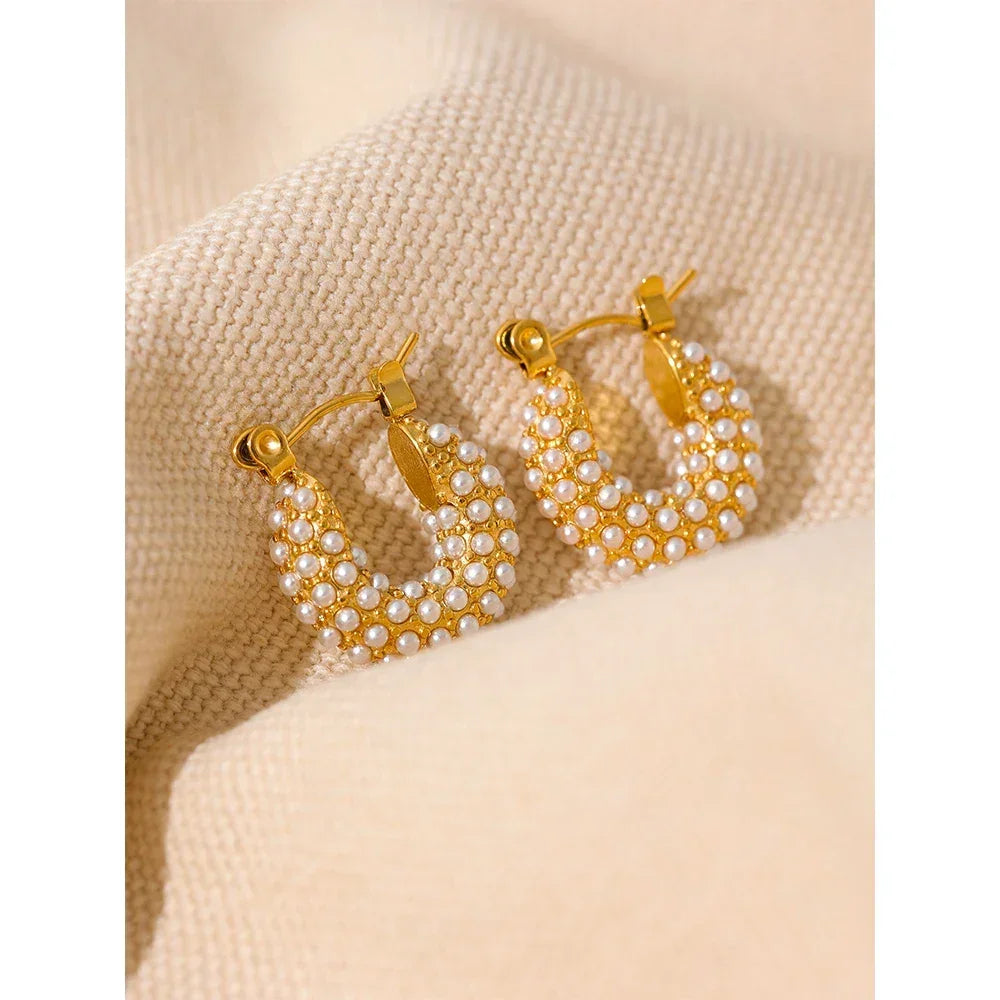 Gold-plated hoop earrings with white pearl accents on a beige fabric background
