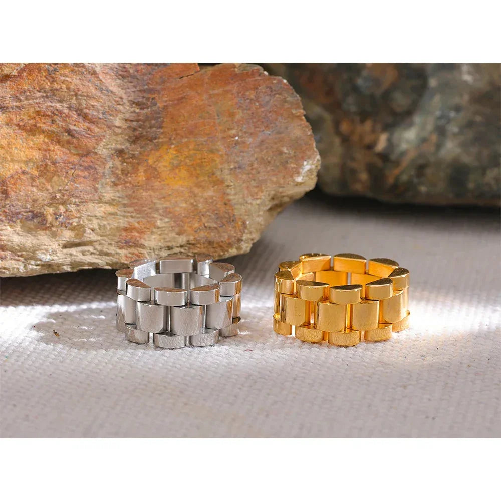 Silver and gold chunky chain rings on textured fabric with natural stone background