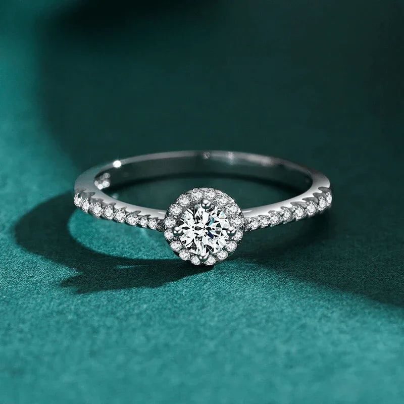 Sterling silver halo engagement ring with round center stone and pavé band on green background