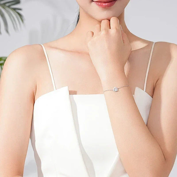 Woman wearing a sterling silver heart charm bracelet with a white sleeveless dress