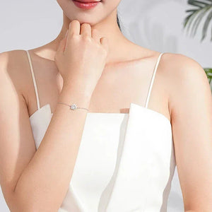 Woman wearing a delicate sterling silver heart bracelet, dressed in a white sleeveless top.