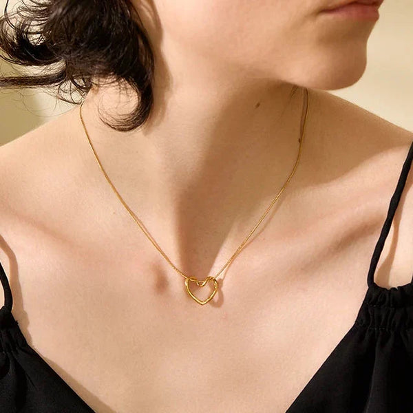 Woman wearing a gold necklace with a minimalistic design, set against a neutral background.