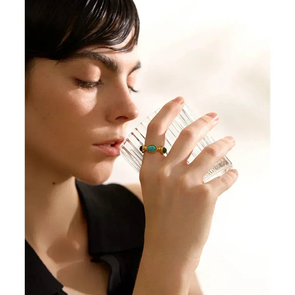 Woman wearing a gold-plated turquoise ring, holding a clear glass, close-up jewelry shot