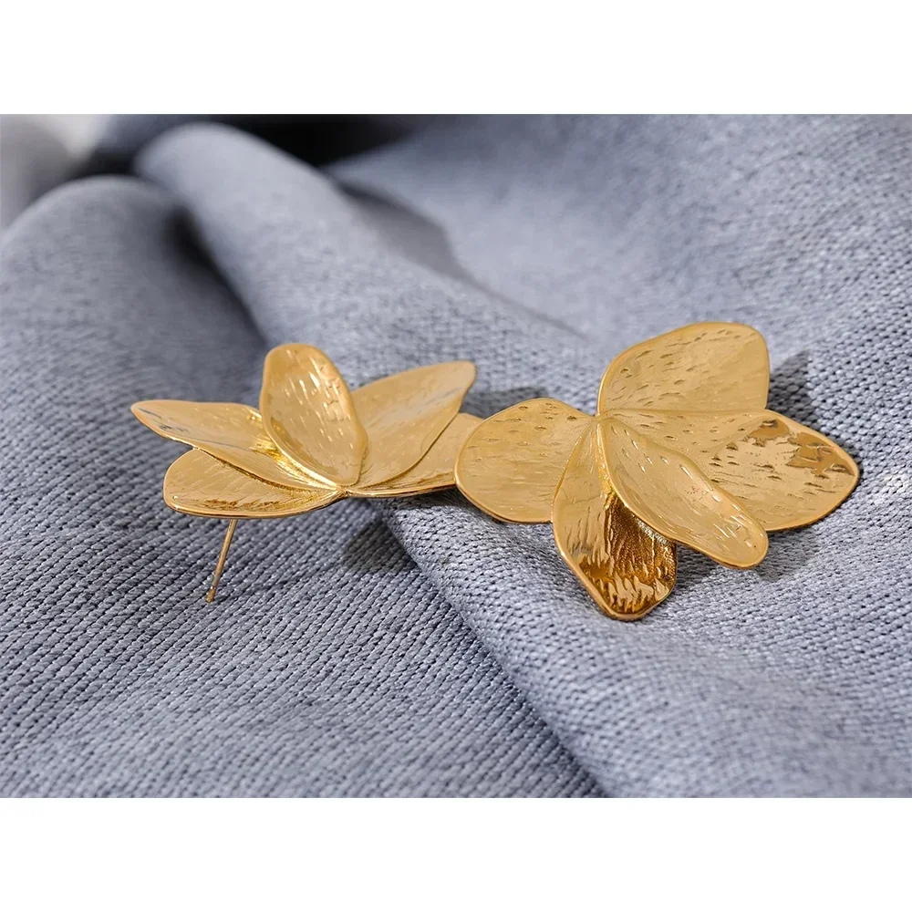 Gold-plated floral earrings with textured petals on a grey fabric background