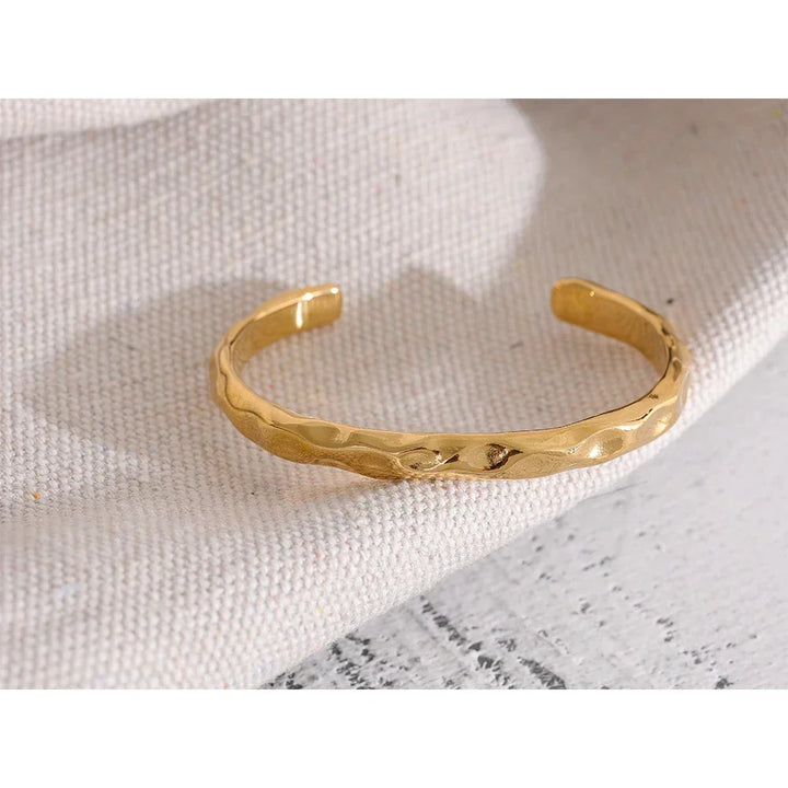 18K gold-plated hammered cuff bracelet on textured fabric background