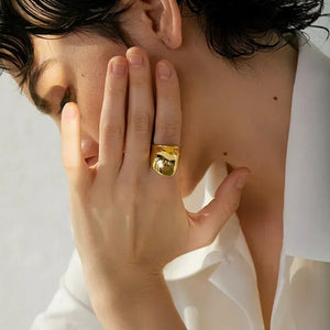 Woman wearing bold gold-plated statement ring, hand near face, white blouse visible