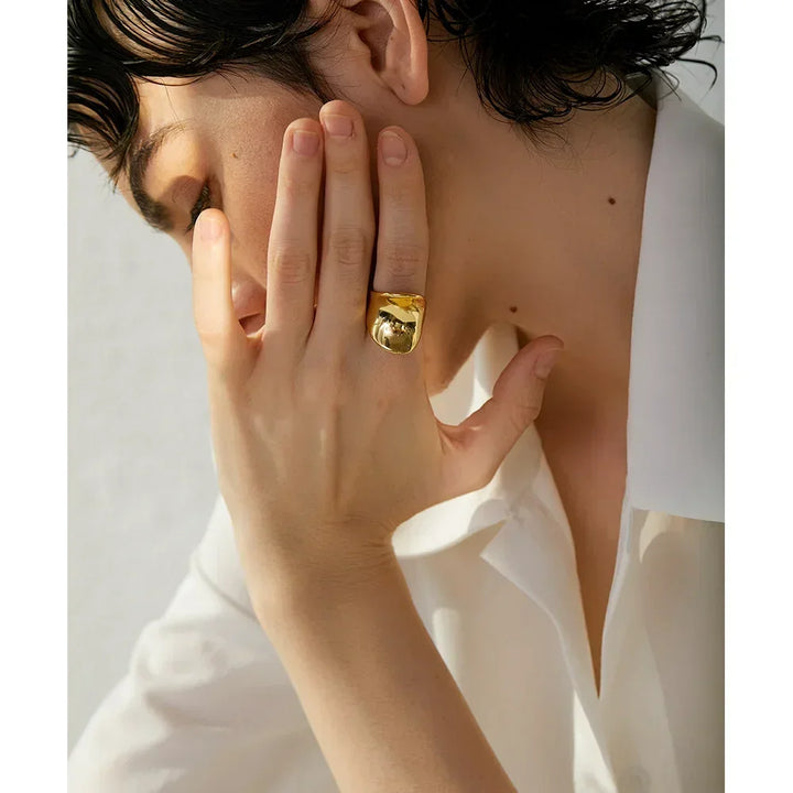 Woman wearing bold gold-plated statement ring, hand near face, white blouse visible