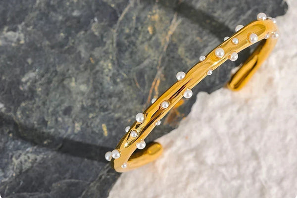 Gold bracelet with pearl-like beads on a stone surface