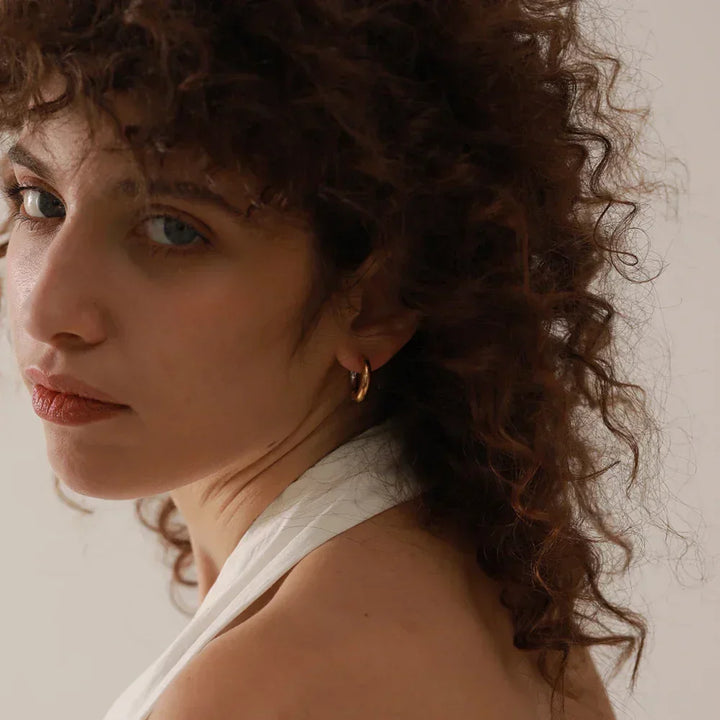 Woman with curly hair wearing a gold hoop earring and white top, minimalist background