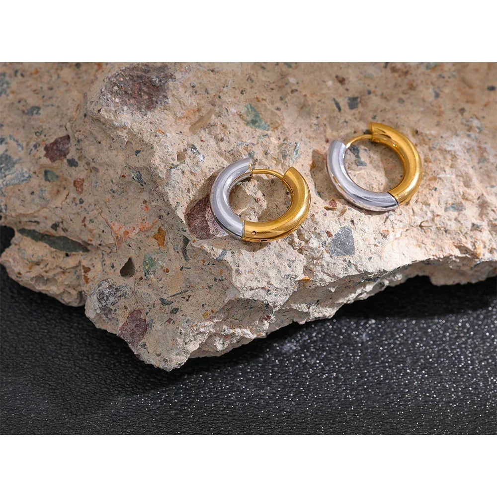 Pair of two-tone gold and silver hoop earrings on a textured stone surface