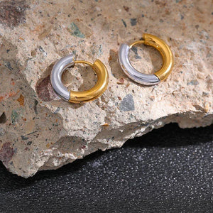 Pair of two-tone gold and silver hoop earrings on a textured stone surface