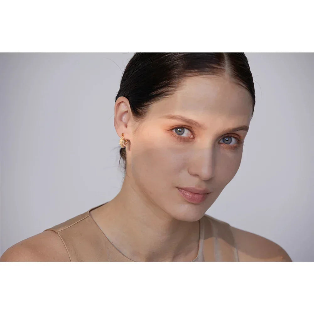 Woman wearing 18K gold-plated textured hoop earrings, minimal makeup, neutral background