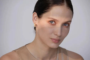 Woman wearing 18K gold-plated textured hoop earrings, minimal makeup, neutral background