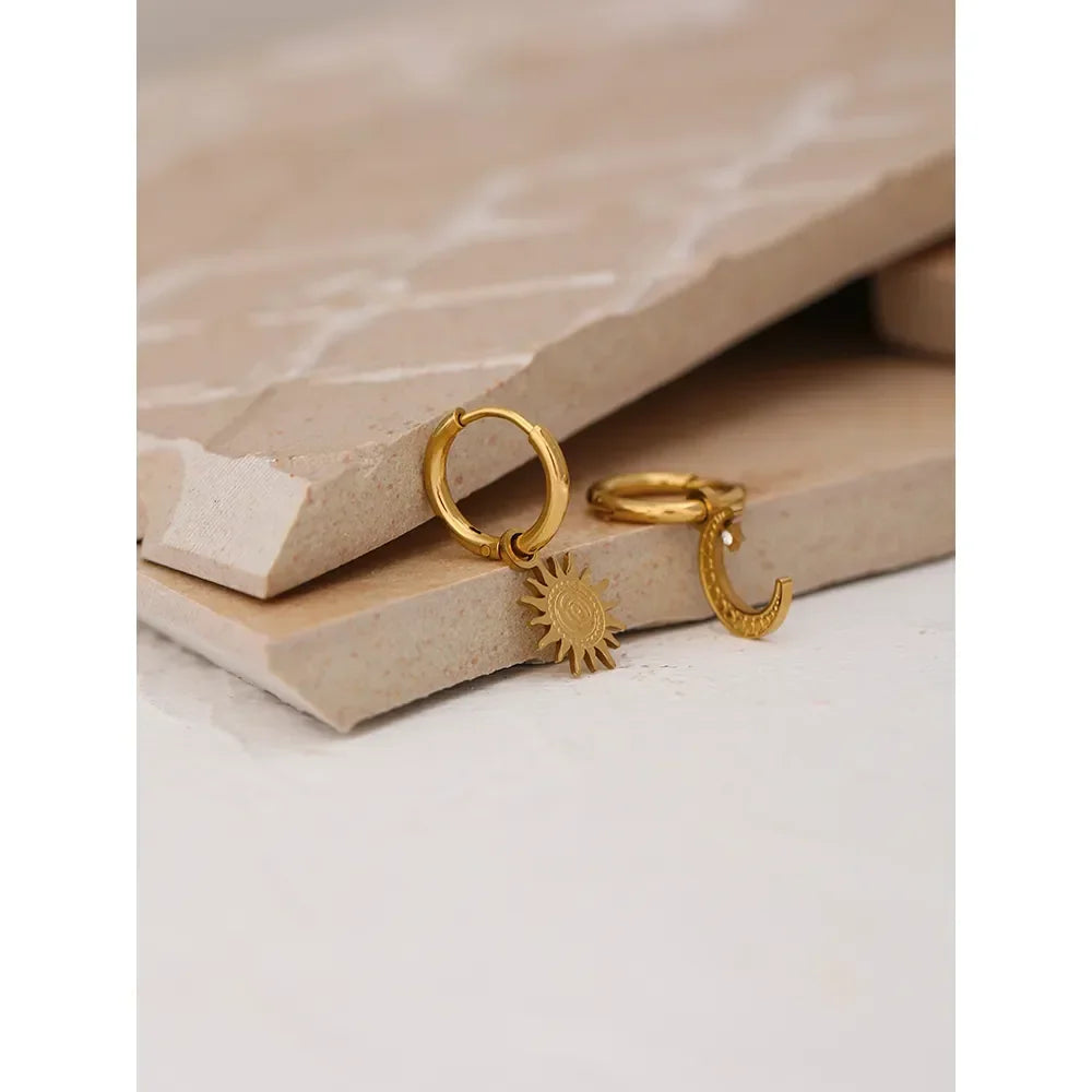 Gold-plated hoop earrings with sun and moon charms on neutral stone background