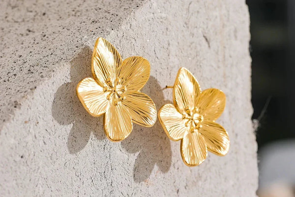 Gold floral earrings on a textured stone surface.