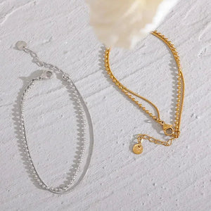Silver and gold-plated chain bracelets with delicate clasps on a textured white surface