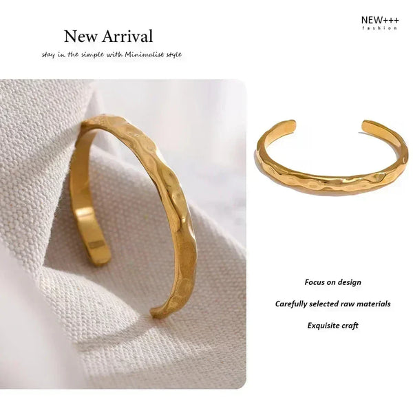 Textured gold-plated open bangle bracelet resting on a neutral fabric surface
