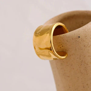 Wide gold-plated ring with hammered texture on a light textured background