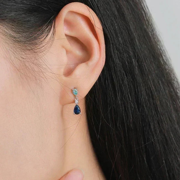 Close-up of an ear wearing a pair of teardrop-shaped earrings with blue gemstones.