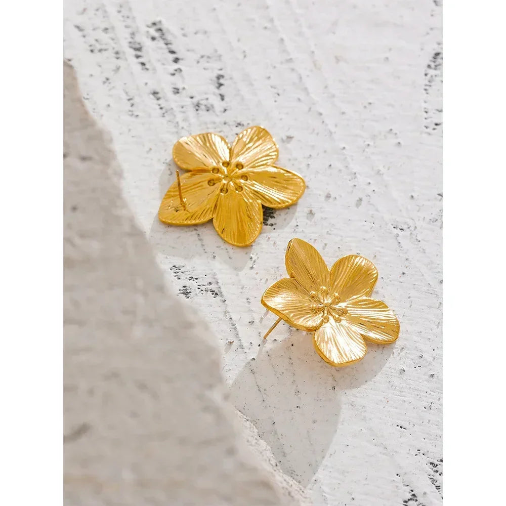 Gold-plated flower stud earrings with textured petals on a light textured surface