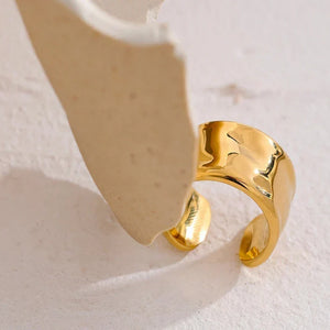 Wide gold-plated ring with hammered texture on a light textured background