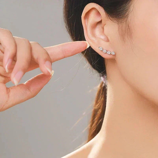 Close-up of a person wearing Dazzling CZ Water Drop Earring a small earring with a hand pointing to it against a neutral background, TM & Co. Jewels
