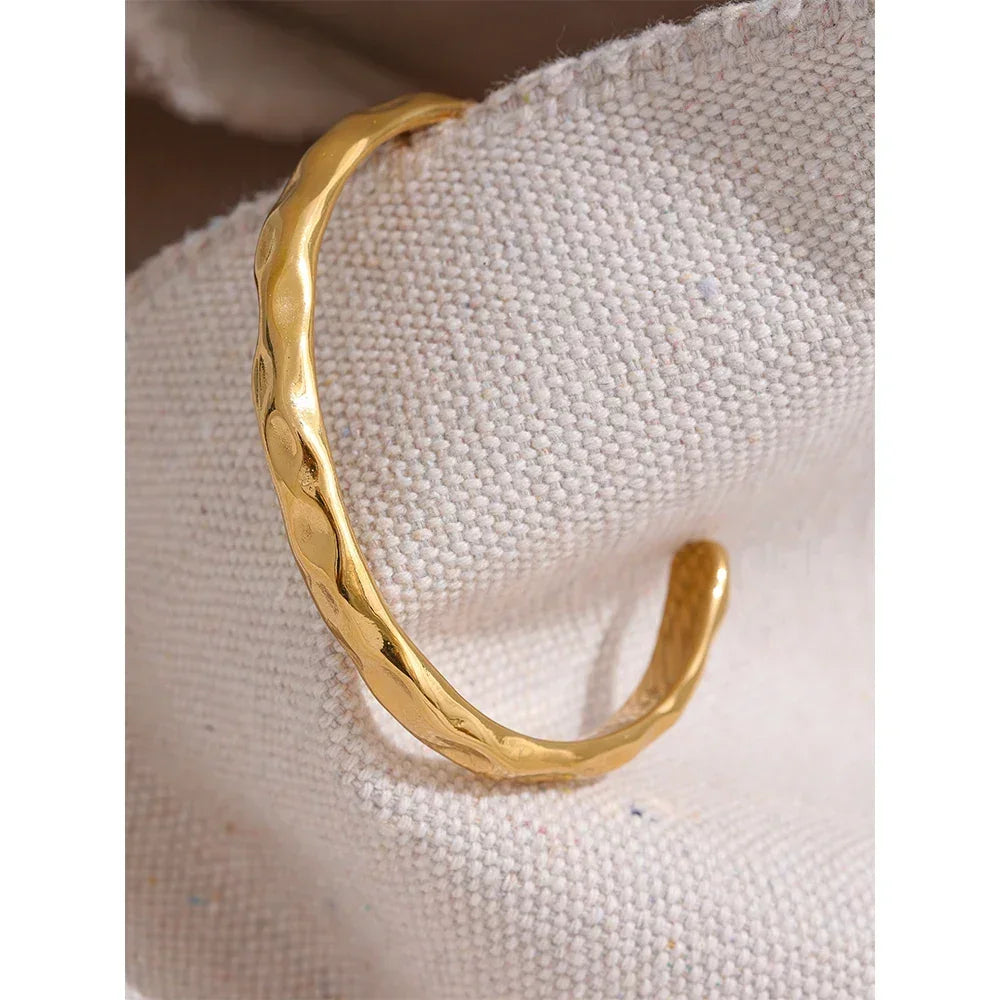 Hammered gold-plated open cuff bracelet on textured fabric background