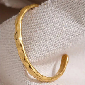 Hammered gold-plated open cuff bracelet on textured fabric background