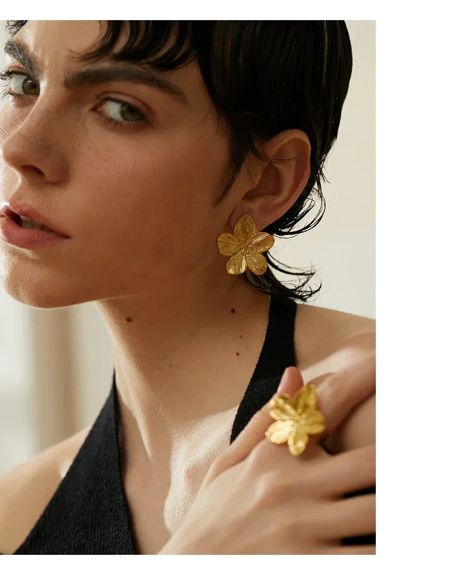 Woman wearing gold-plated flower-shaped statement earrings and matching ring