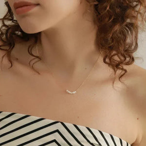 Woman wearing a delicate gold-plated necklace with small pearls, striped top, curly hair