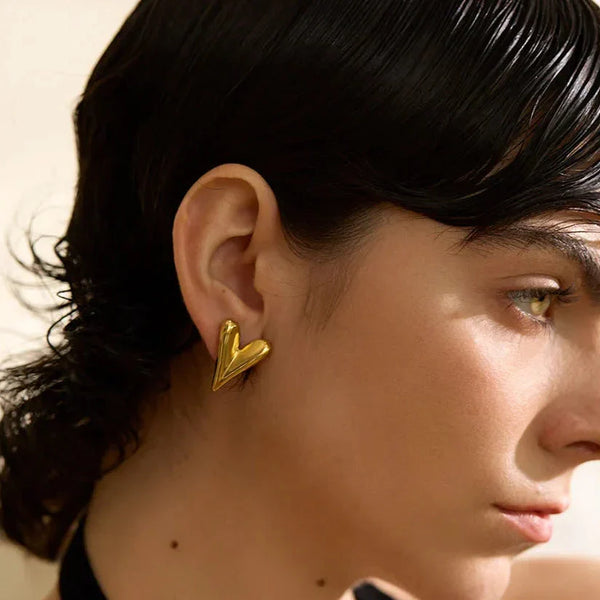 Close-up of a person wearing a gold heart-shaped earring against a neutral background