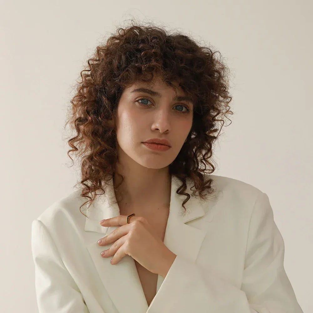 Woman in a white blazer wearing a gold-plated ring, neutral background