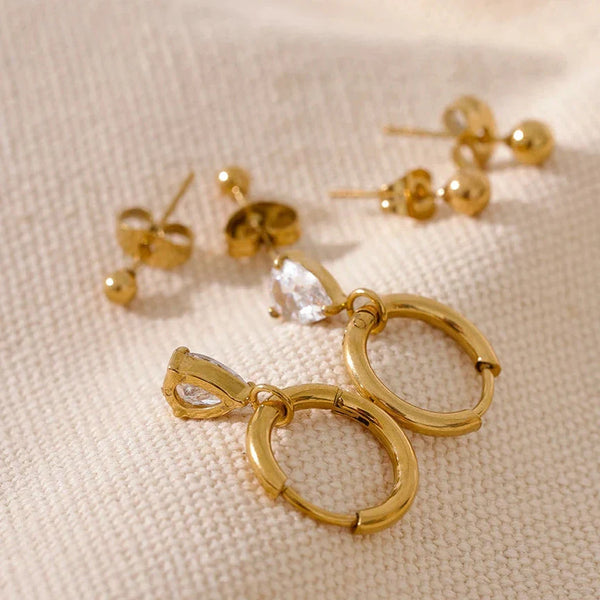 Gold hoop earrings with clear stones on a beige fabric background
