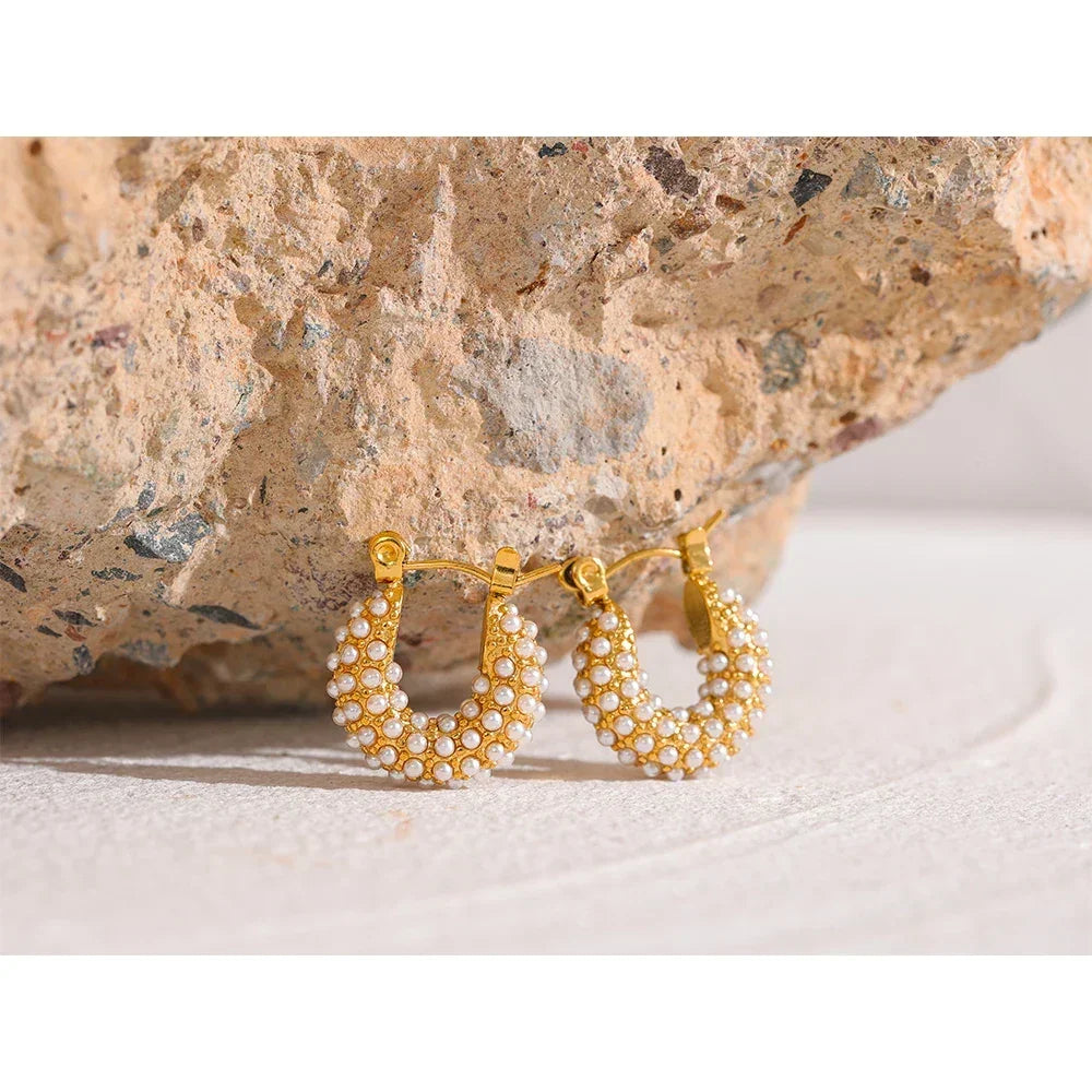 Gold-plated hoop earrings with white pearls on textured stone background