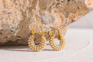 Gold-plated hoop earrings with white pearls on textured stone background