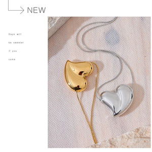 Heart-shaped gold and silver pendants on a textured surface with 'NEW' text.