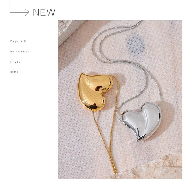 Heart-shaped gold and silver pendants on a textured surface with 'NEW' text.