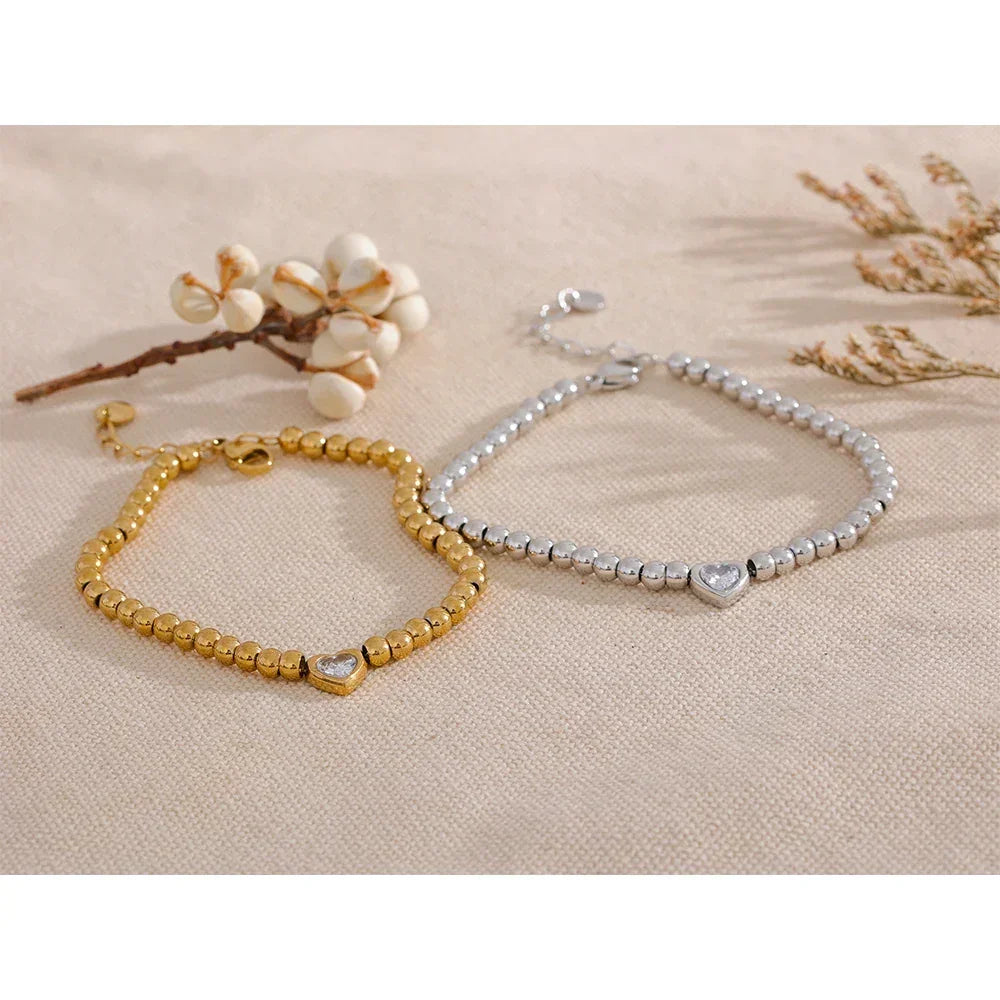 Gold and silver beaded bracelets with heart charms on a beige fabric background