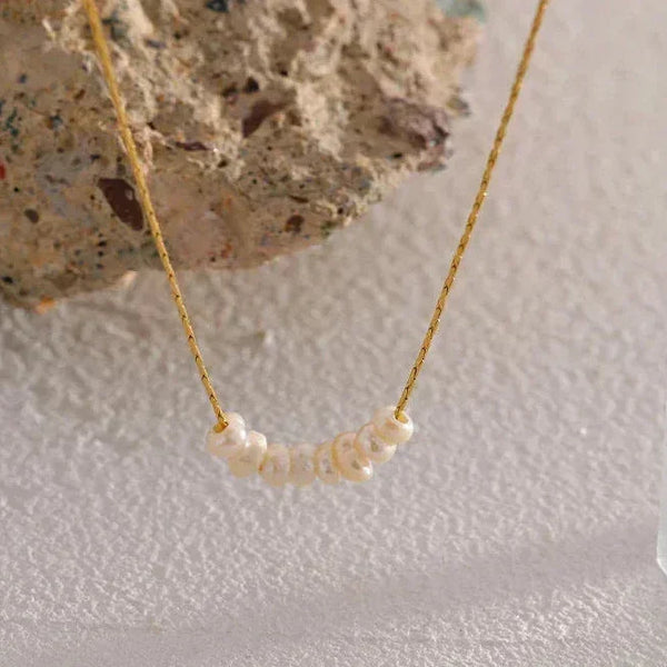 Delicate gold necklace with small natural pearls on textured stone background