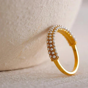 Gold-plated ring with rows of small pearls on textured beige fabric background