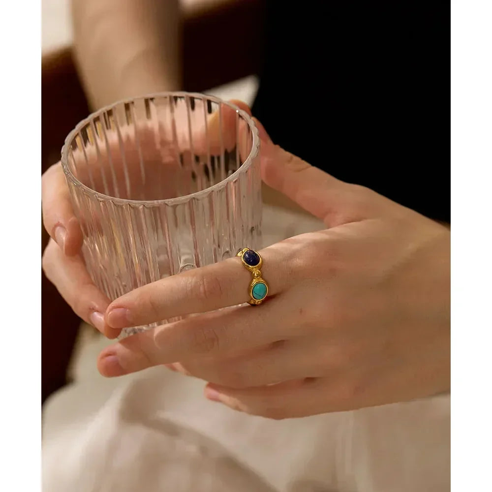 Woman wearing a gold-plated silver ring with blue and turquoise stones, holding a glass
