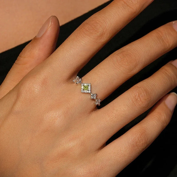 Close-up of a hand wearing a diamond ring with a green gemstone on a neutral background-TM & CO. JEWELS 