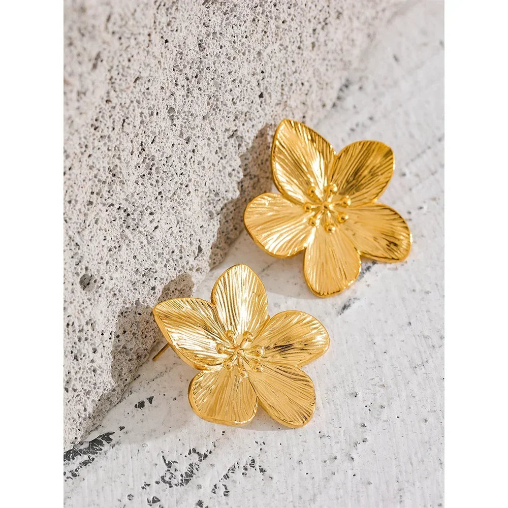 Gold-plated flower-shaped earrings on textured stone surface, elegant jewelry accessory