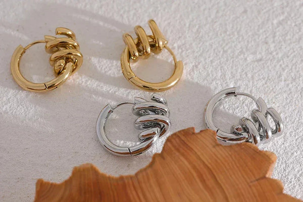 Gold and silver hoop earrings with spiral twist design on textured white surface